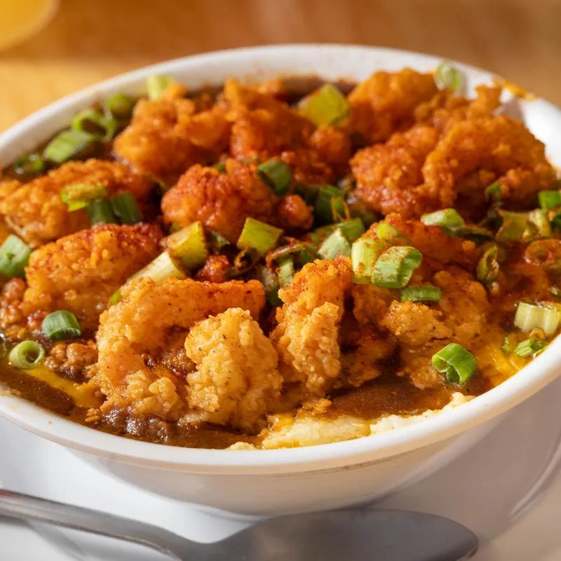 A bowl of fried shrimp and grits topped with gravy and green onions